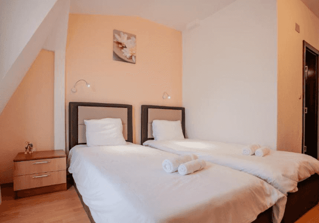 Twin beds with white linens and rolled towels in a hotel room with peach walls.