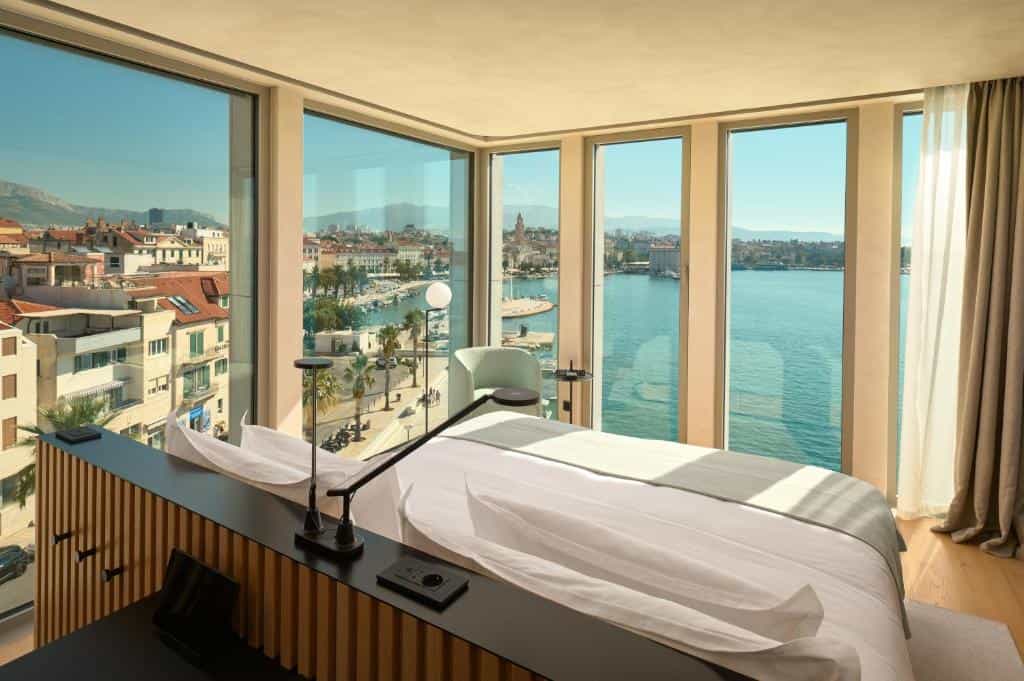 Hotel room with large windows overlooking a coastal city and blue sea water