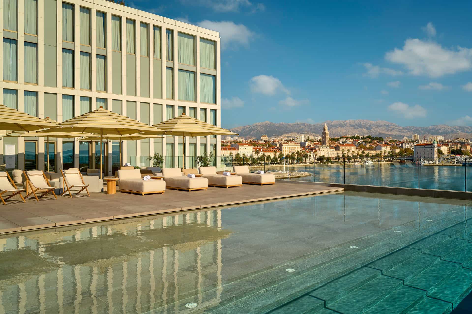 Rooftop pool deck with lounge chairs overlooking the historic city of Split and mountains.