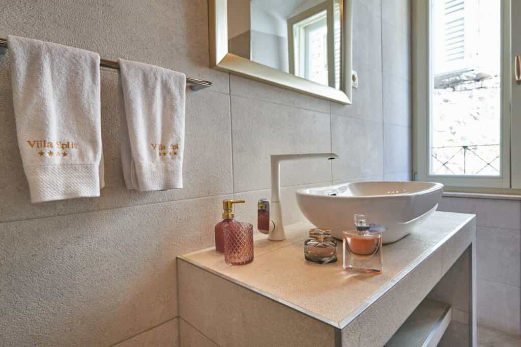 Bathroom vanity with vessel sink, white towels embroidered "Villa Split," and perfume bottles.