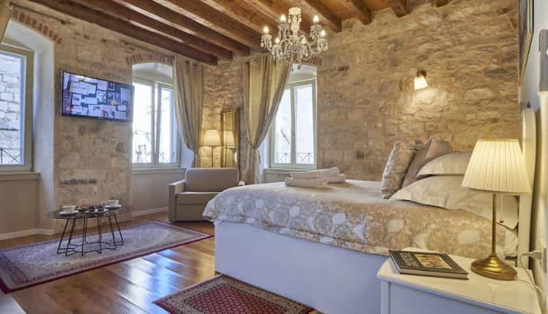 Bedroom with stone walls, wood beams, chandelier, and large bed in historic building.