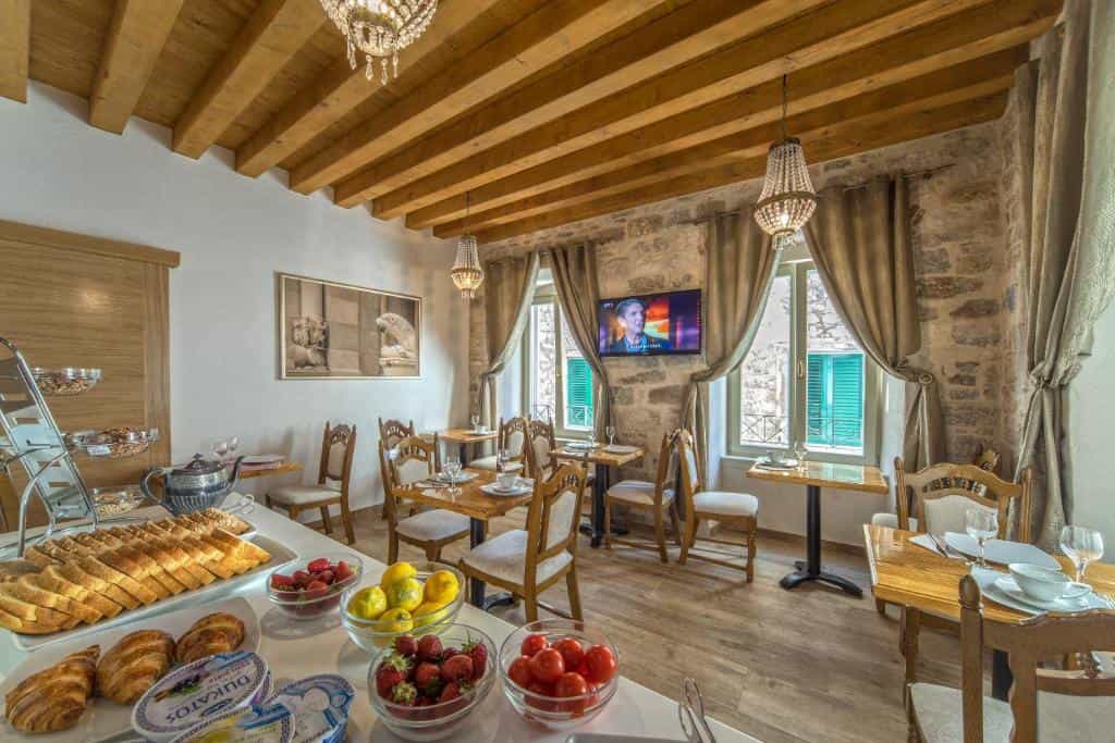 Breakfast buffet with bread, fruit, and pastries set in a room with stone walls and wood beams.