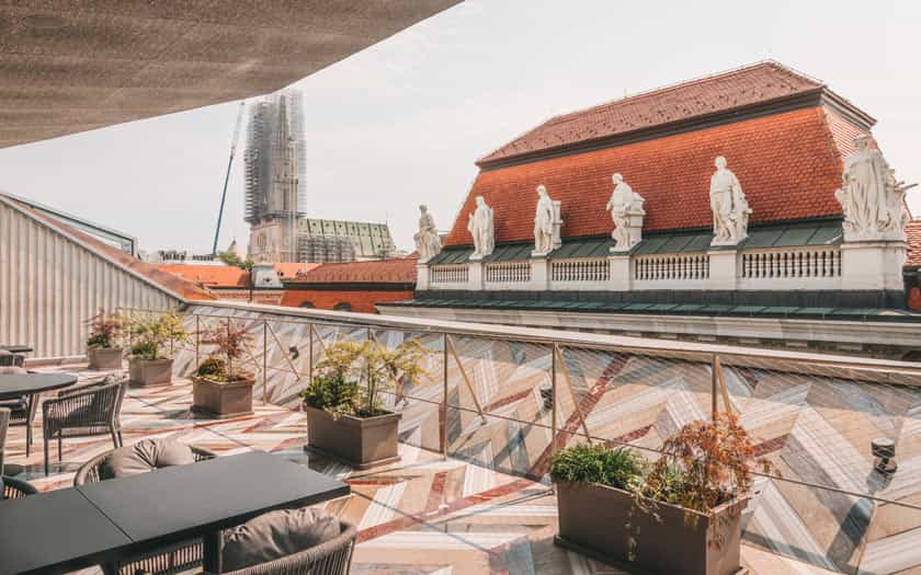 Rooftop terrace with outdoor seating overlooking historic buildings and a church tower under construction in Zagreb.