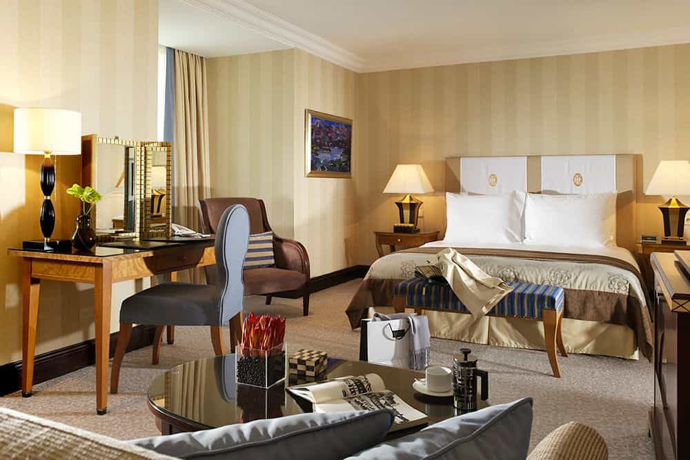 Hotel bedroom with striped wallpaper, large bed, desk, and seating area, likely in Zagreb.