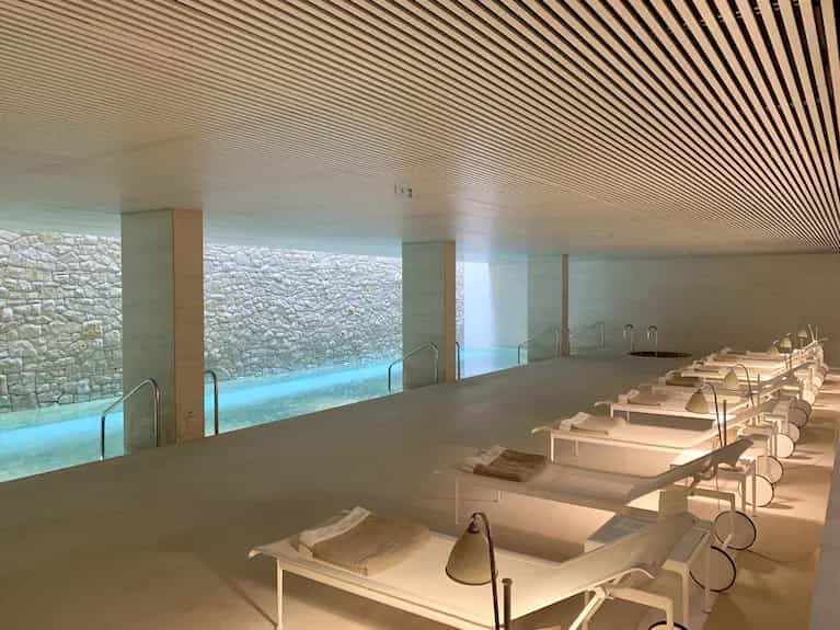 Indoor pool area with stone walls, white lounge chairs, and slatted ceiling at Square Hotel Belgrade.