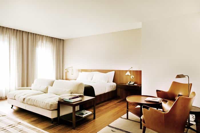 Modern hotel room with white bedding, light sofa, and brown leather chairs in Square Nine Hotel Belgrade.