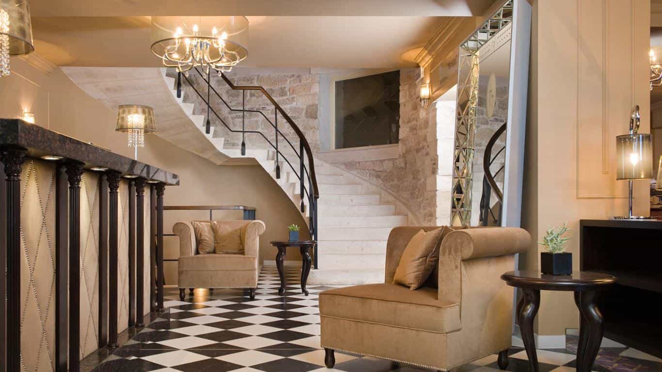 Hotel reception area with curved staircase, plush seating, and black and white checkered floor.