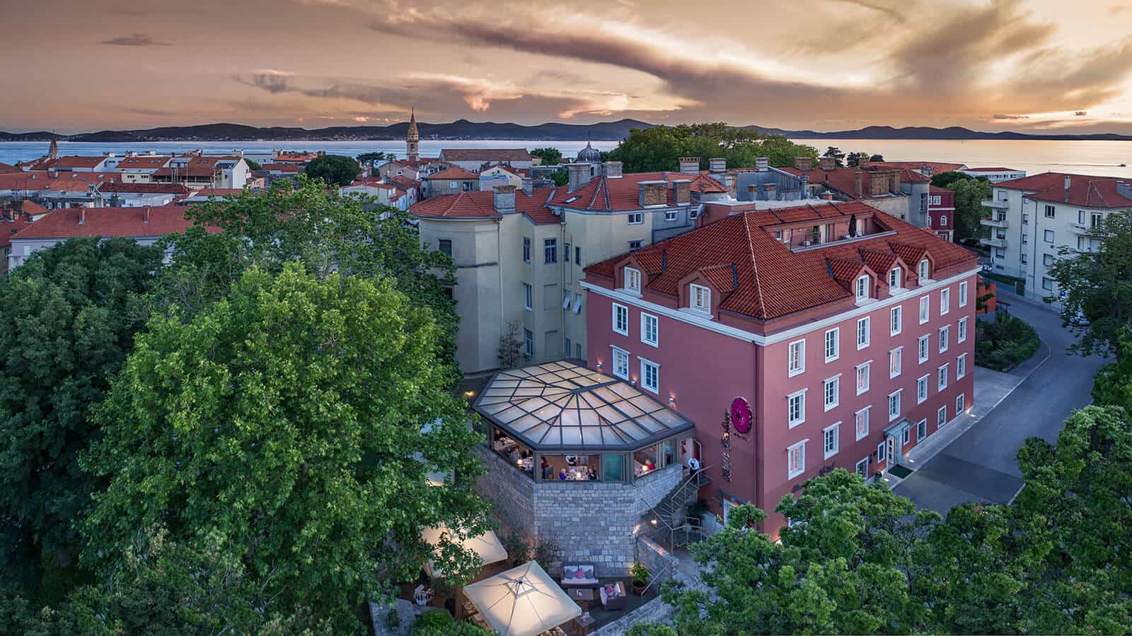 Hotel Bastion Zadar building with red tile roofs overlooking the sea at sunset.