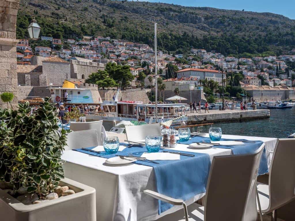 Outdoor dining table overlooking harbor with boats and Dubrovnik hillside houses