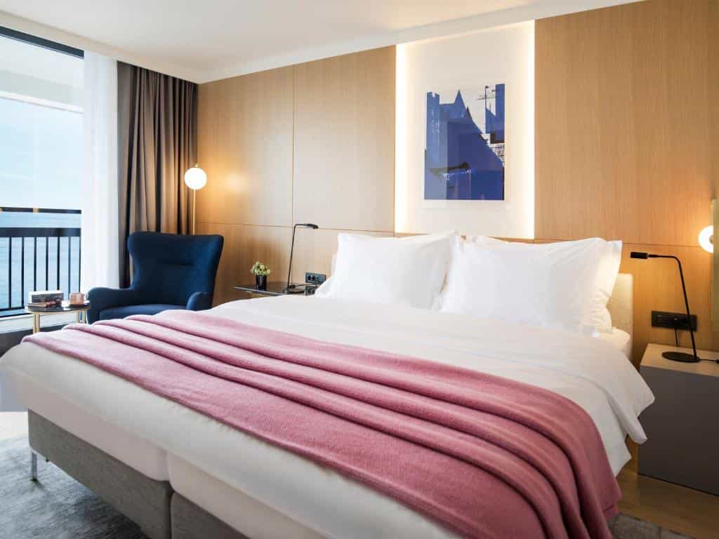 Bedroom with large bed, blue chair, and sea view balcony at Hotel Excelsior Dubrovnik.