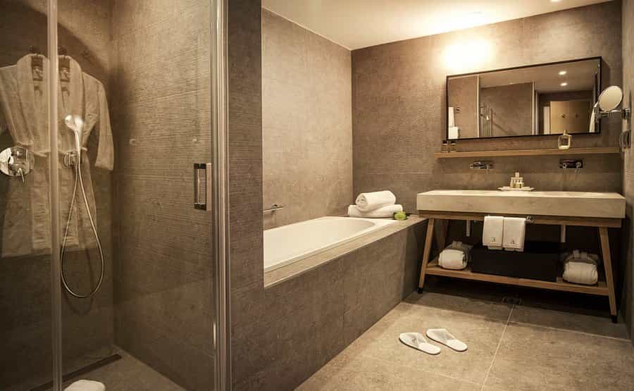 Modern hotel bathroom with glass shower, bathtub, wood vanity, and white slippers in Dubrovnik.