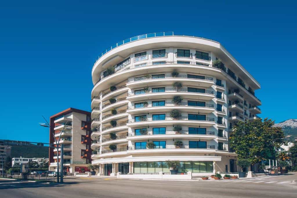 Curved white hotel building with balconies and blue sky, near mountains.
