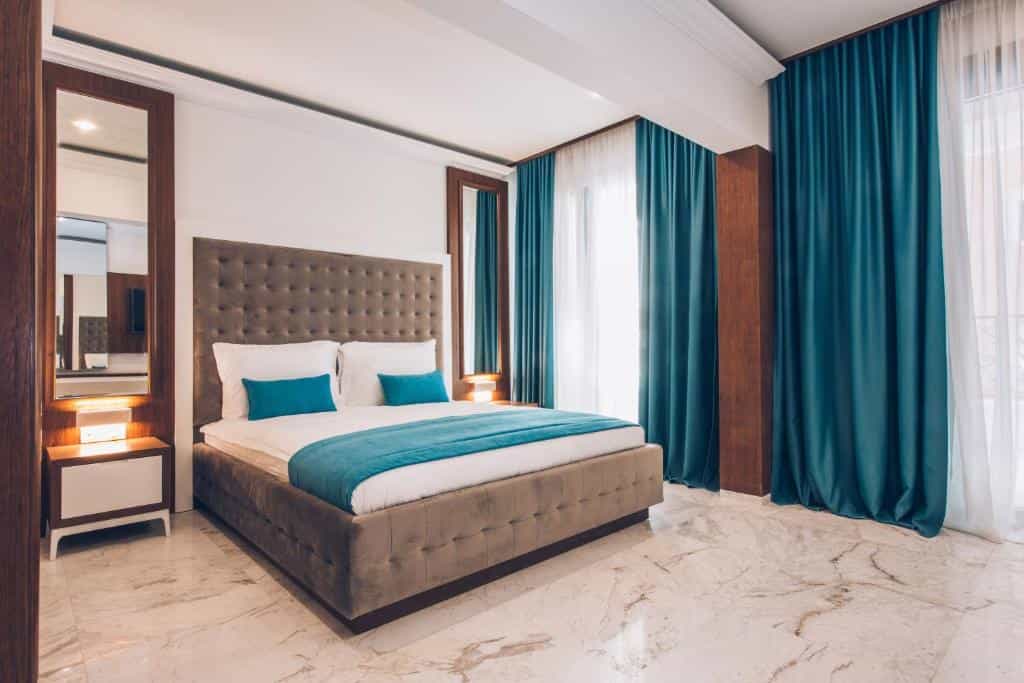 Hotel bedroom with tufted headboard, white bedding, and teal accents, featuring marble floor.