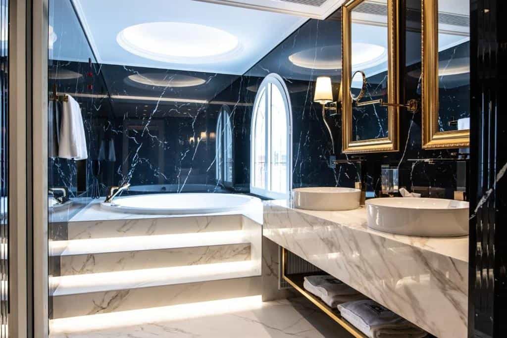 Luxury bathroom with black marble walls, white marble vanity, soaking tub, and gold accents at Xheko Imperial Hotel Tirana.
