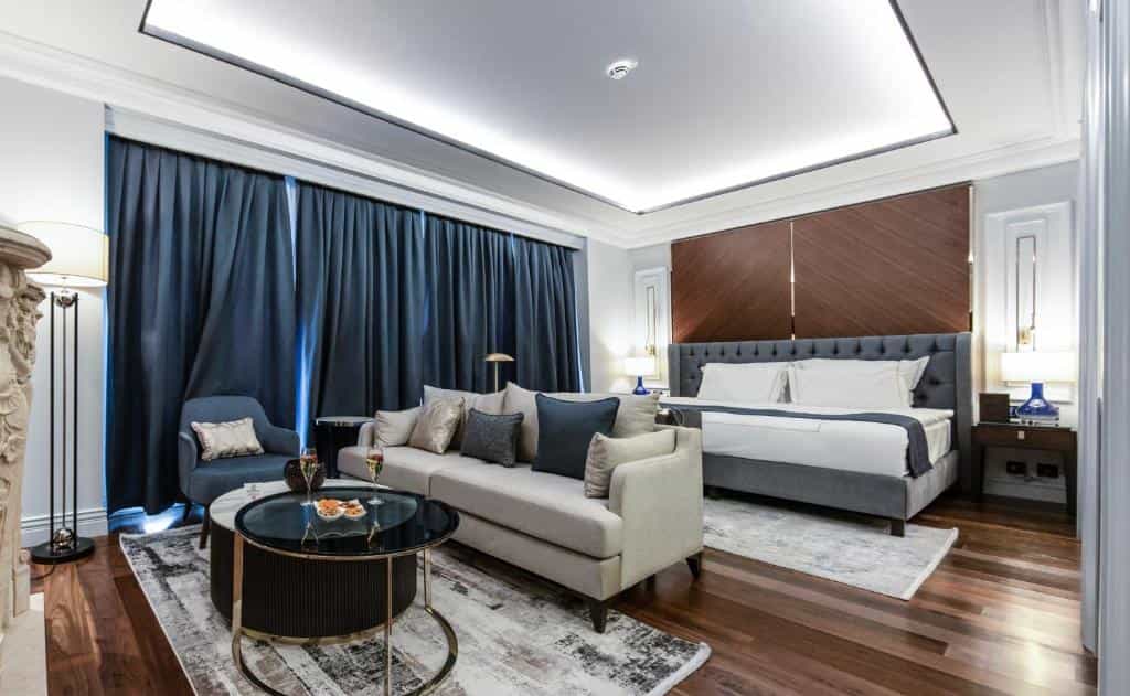 Luxury hotel suite with king bed, sofa, coffee table, and dark blue curtains in Tirana.