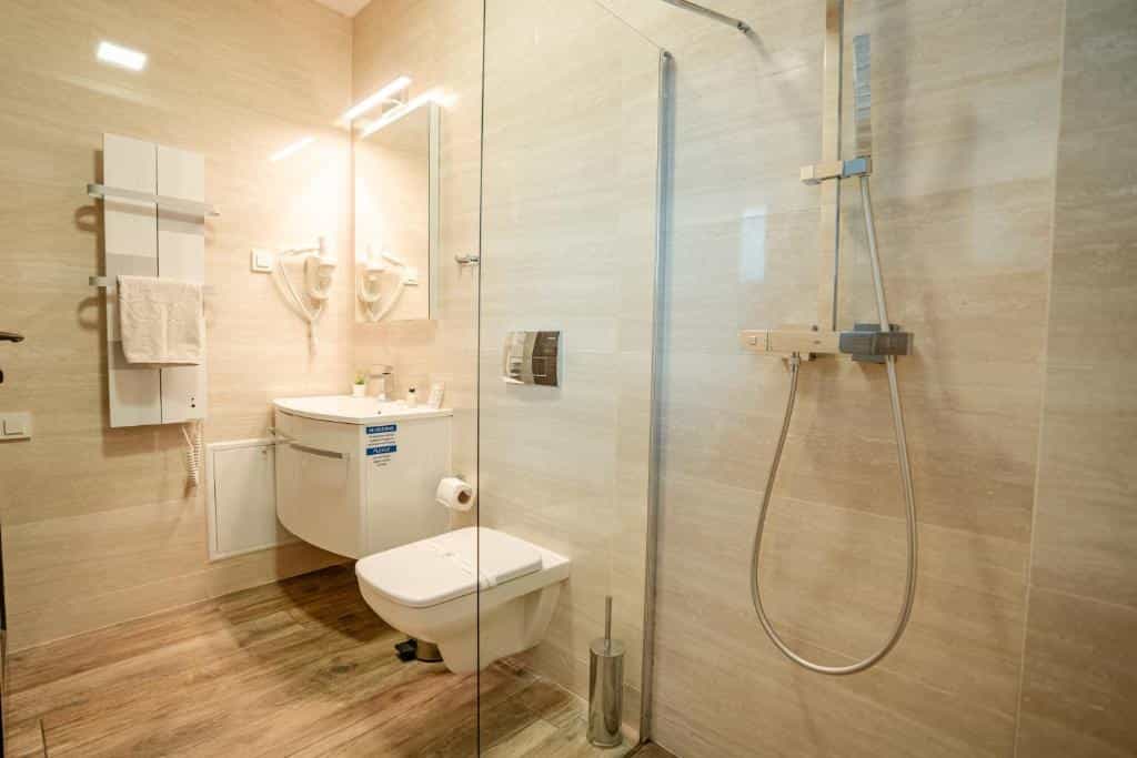 Modern hotel bathroom with beige tile, vanity, toilet, and glass shower stall. Vila Sofia Ohrid.