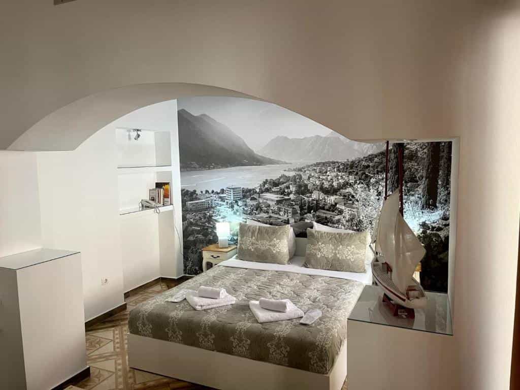 Bedroom with bed, model sailboat, and black and white mural of a coastal town and mountains.