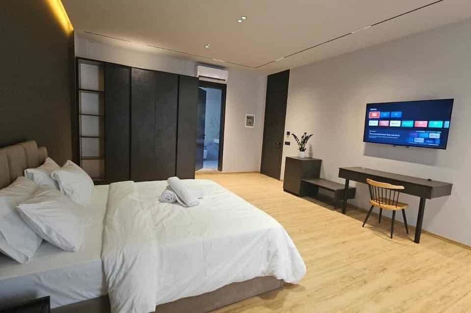 Modern hotel bedroom with white linens, dark furniture, and wall-mounted television in Shkoder.