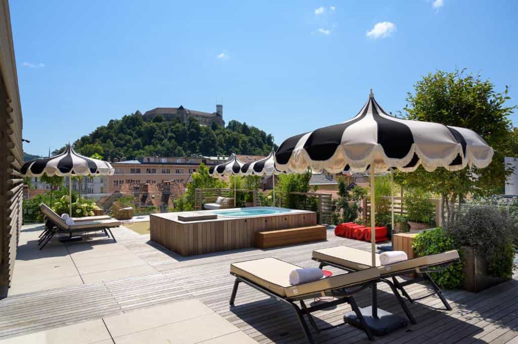 Rooftop terrace with hot tub, lounge chairs, and black-and-white umbrellas overlooking Ljubljana Castle.