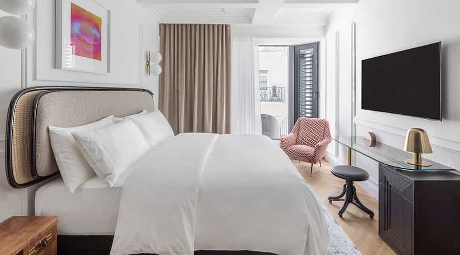 Boutique hotel room with white bedding, modern furnishings, and balcony access in Ljubljana.