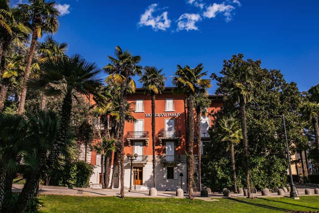 Hotel Sv. Jakov building seen through tall palm trees on a sunny day