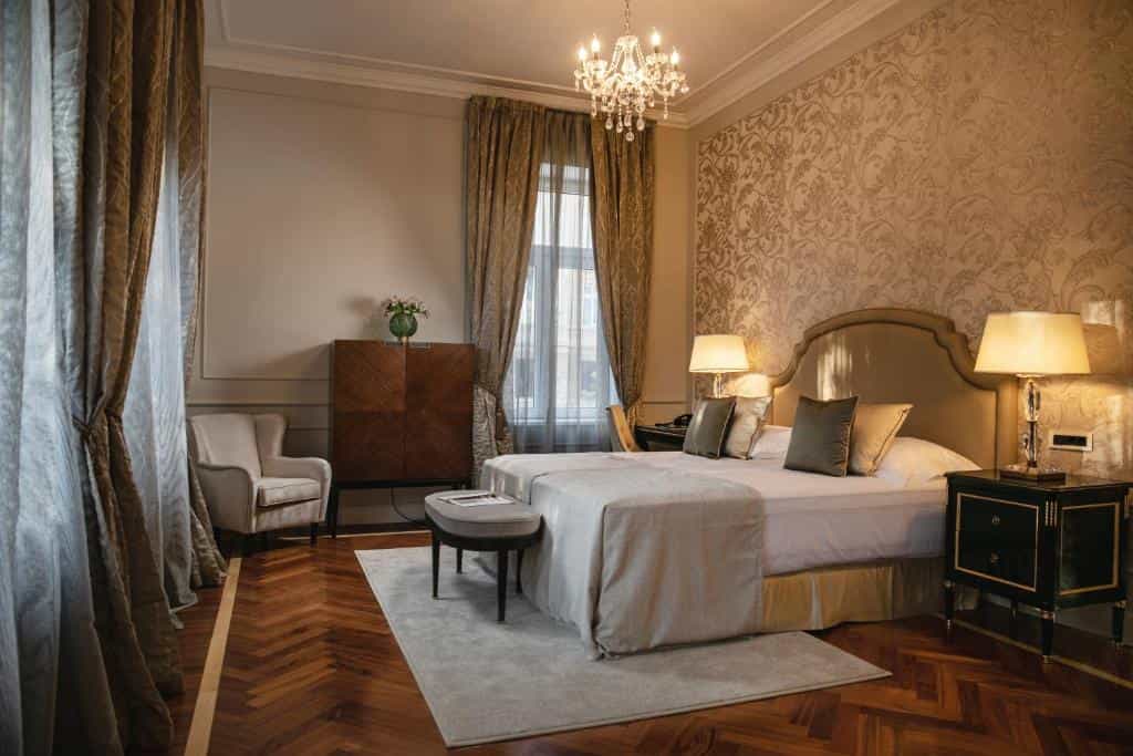 Luxurious hotel bedroom with ornate wallpaper, chandelier, and herringbone wood floor