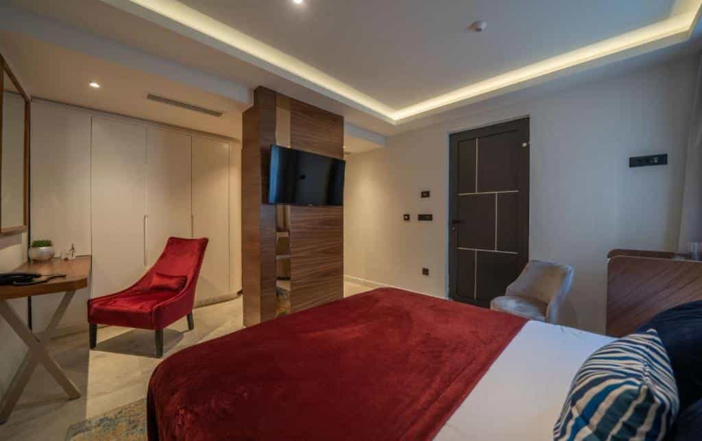 Hotel room with red velvet bedding, modern wood paneling, and a red lounge chair in Kotor.