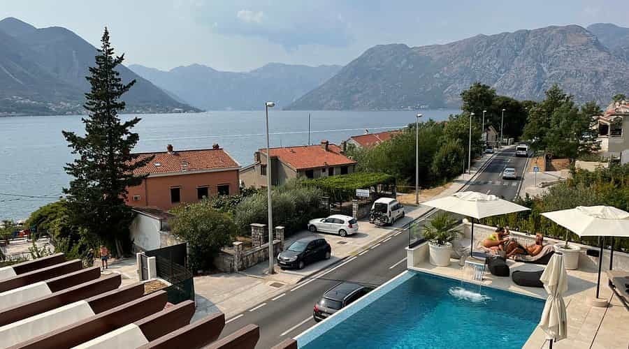 Infinity pool terrace overlooking a bay with mountains, road, and houses in Kotor.