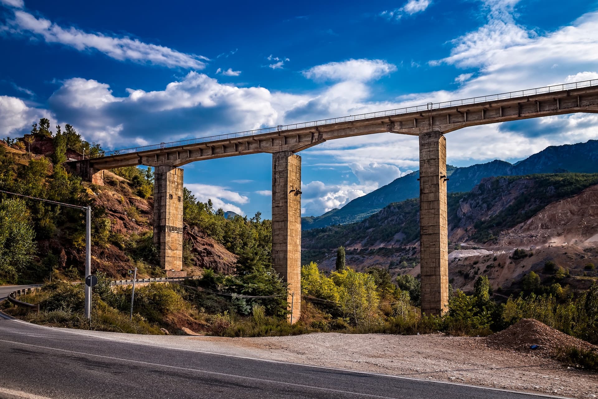 Abandoned railway viaduct crossing a valley with mountains under a dramatic blue sky.