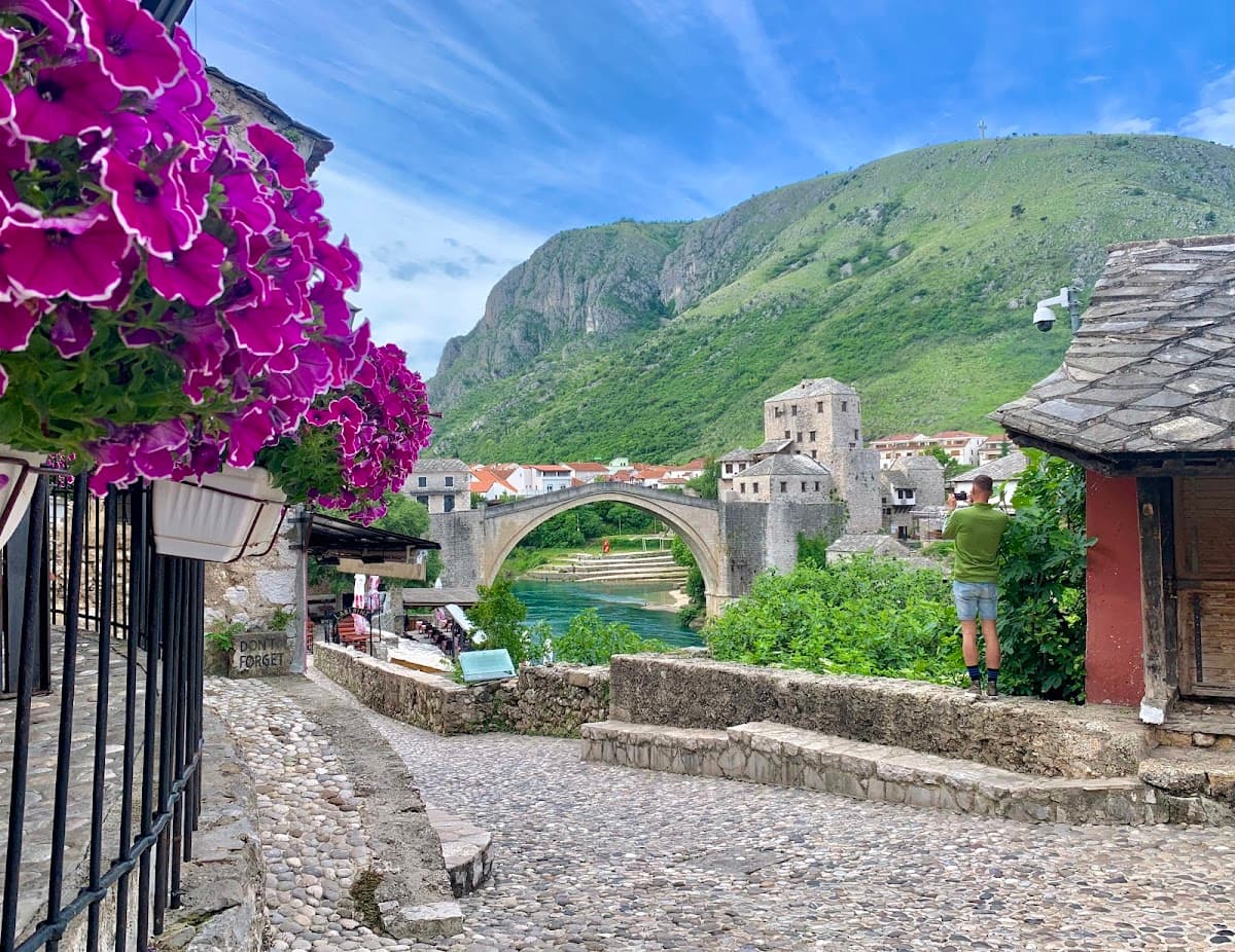 Cobblestone path leading to Stari Most bridge with green mountains in Mostar, Bosnia and Herzegovina.