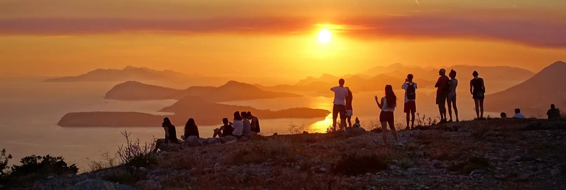 Group watching sunset over hazy mountains and coastal islands from rocky overlook