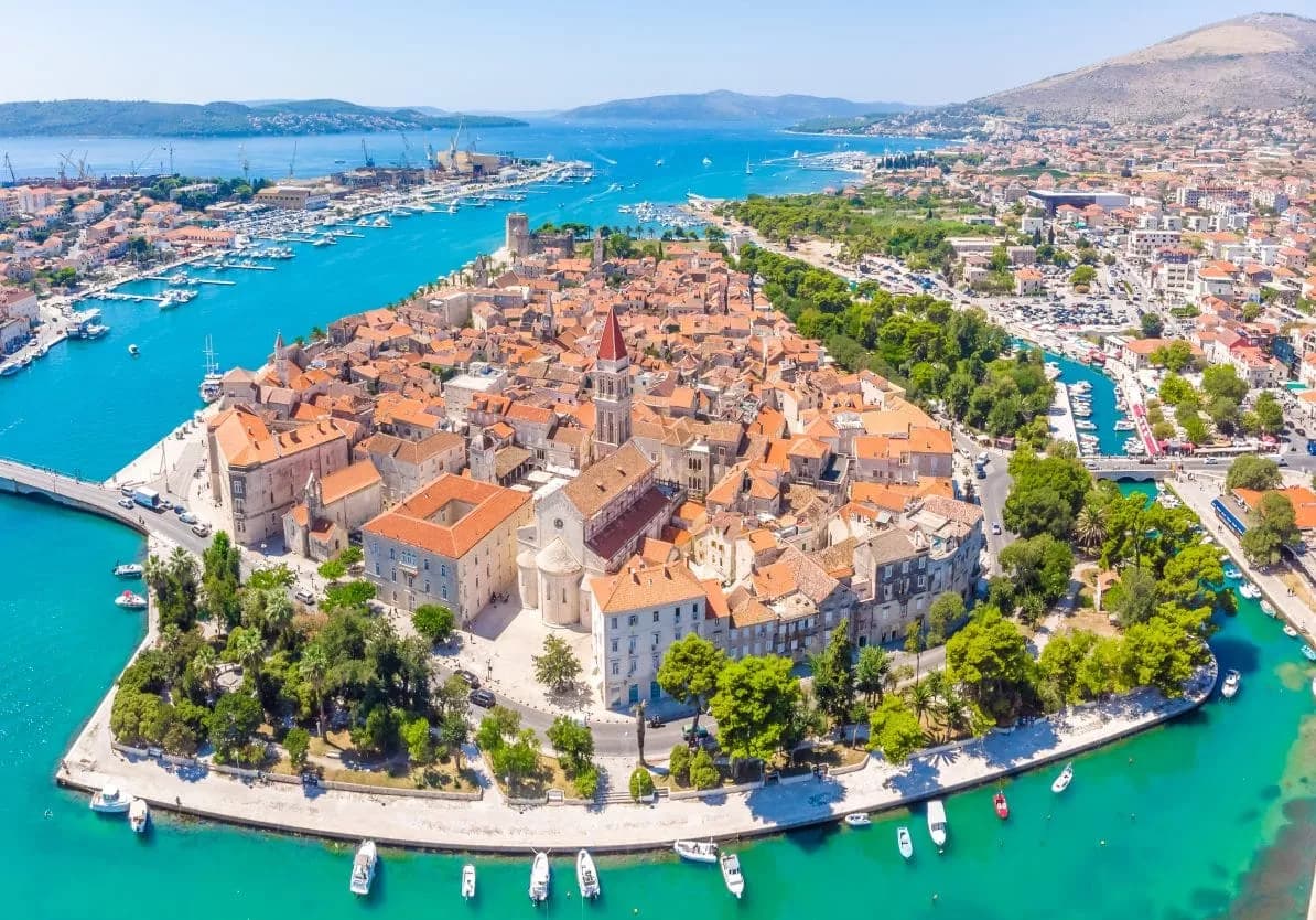 Aerial view of Trogir historic town center with terracotta roofs surrounded by turquoise sea.