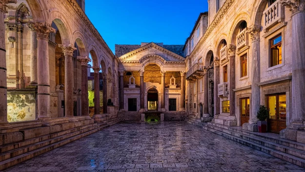 Romanesque courtyard with stone columns and arches illuminated at dusk, Split heritage site.