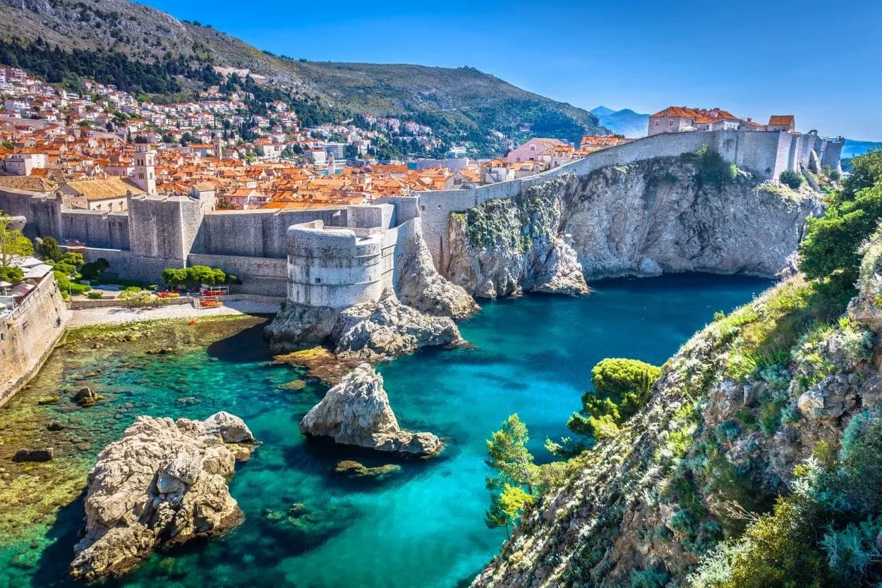 Dubrovnik city walls overlooking turquoise Adriatic Sea cove with rocky coastline