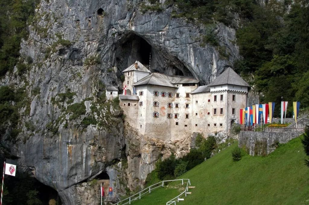 Predjama Castle built into a massive cave entrance in a steep rock face with green hillside.