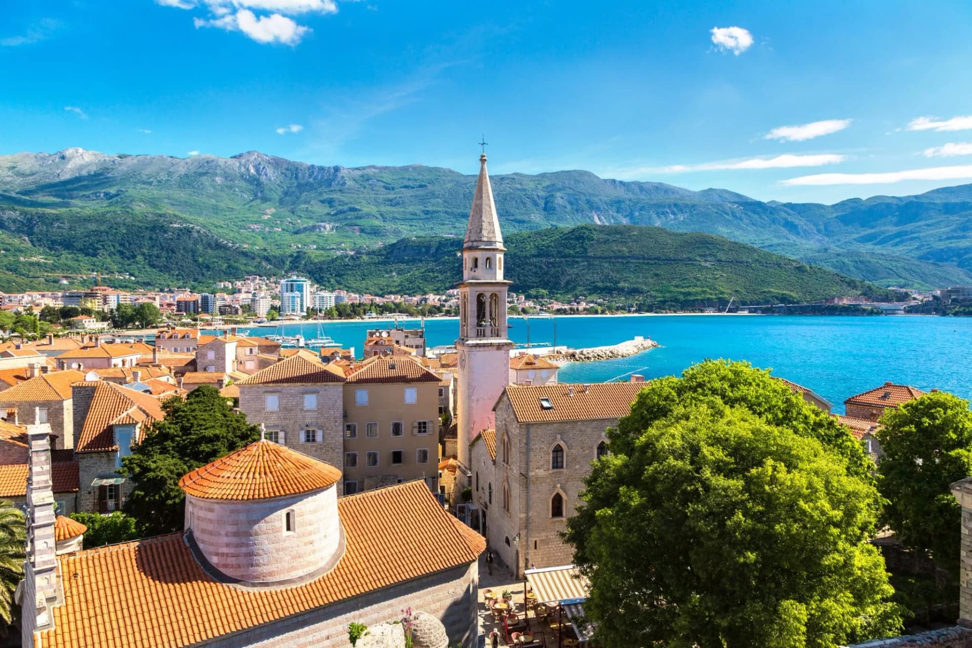 Rooftops of Budva old town, bell tower, and mountains overlooking bright blue Adriatic Sea.