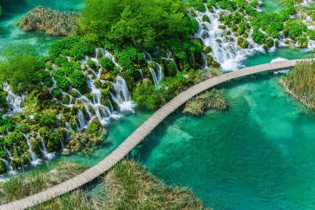 Wooden boardwalk over turquoise pools and waterfalls in National Park of Plitvice Lakes.