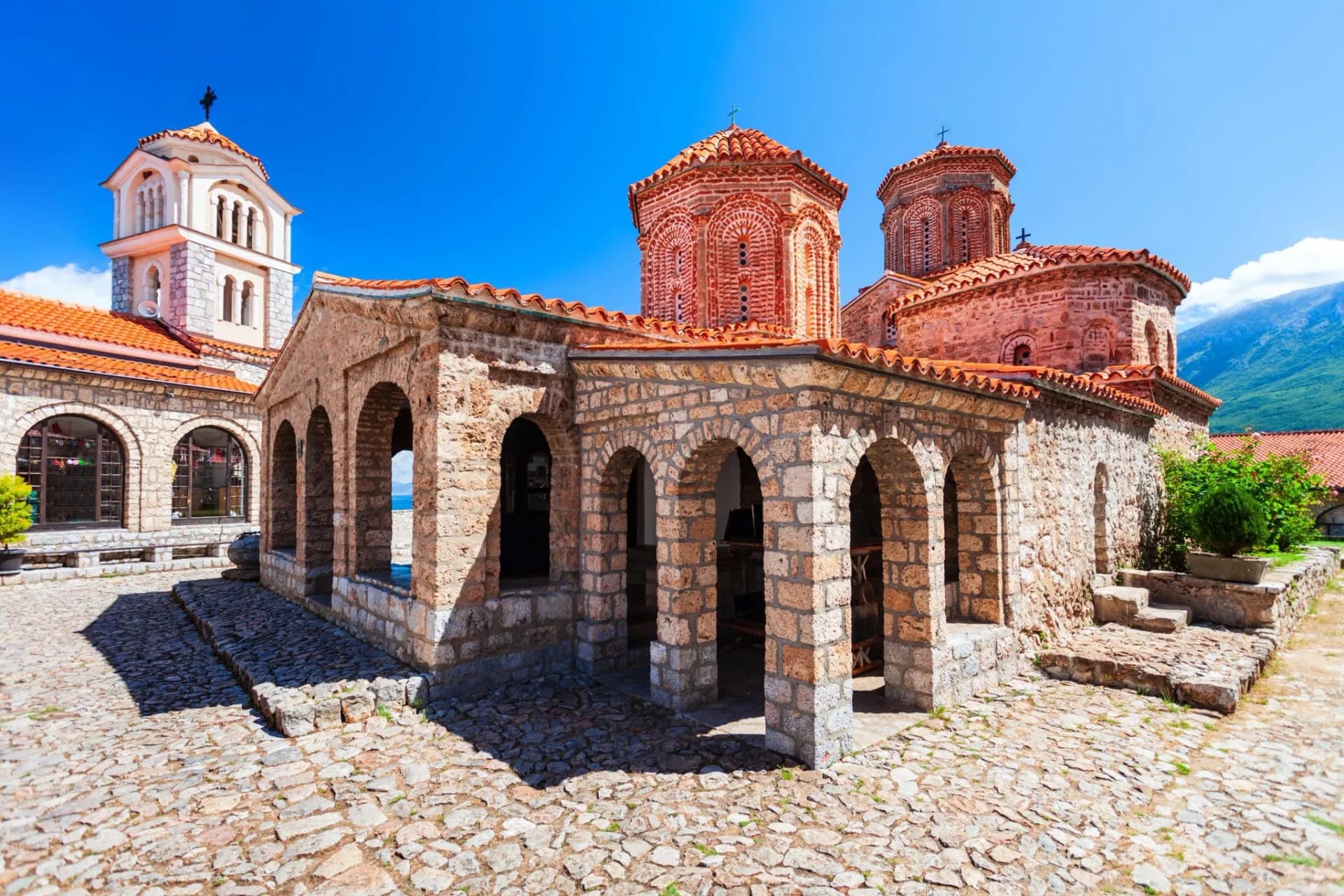 St. Naum monastery stone arches, red tile roofs, and bell tower under bright blue sky.