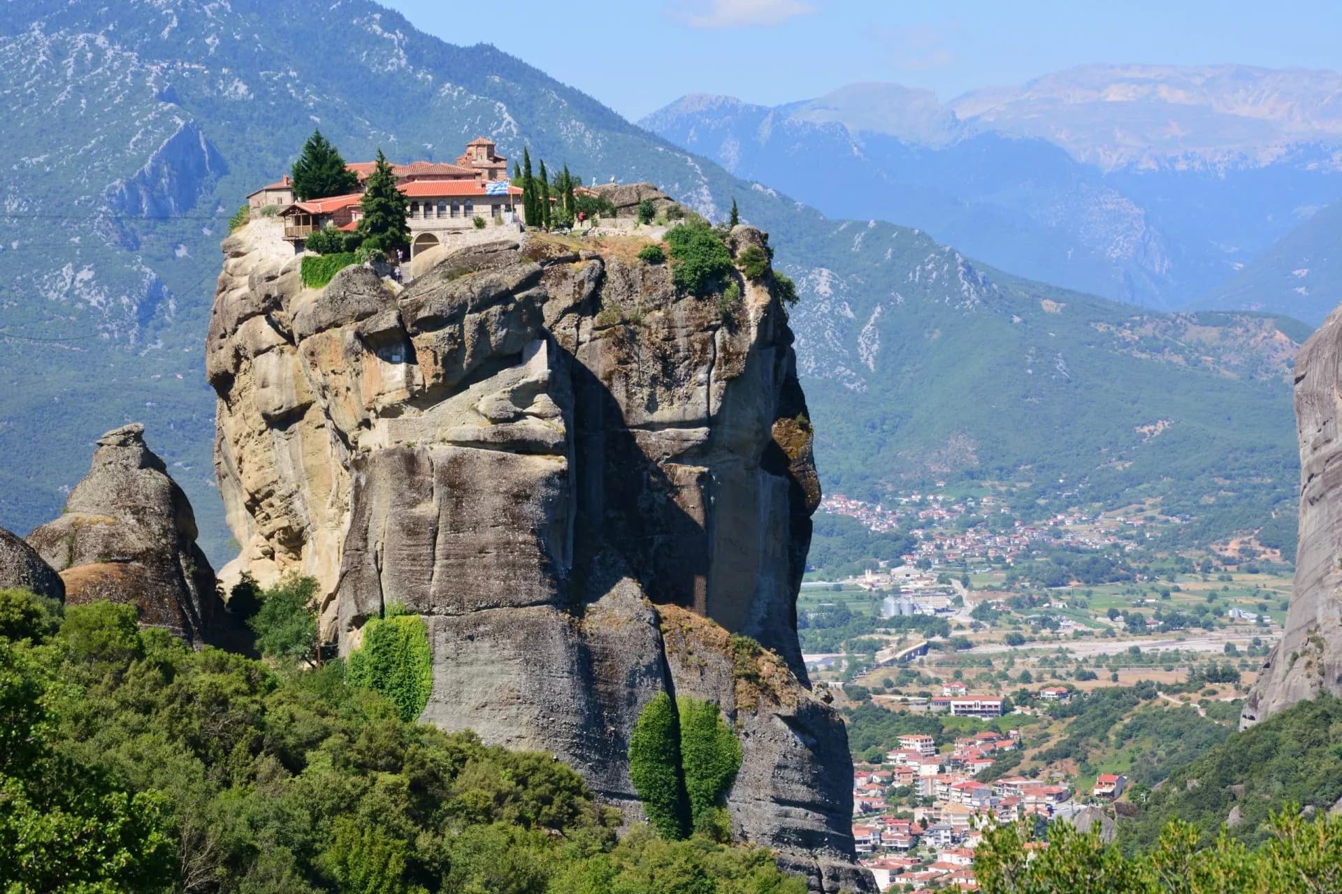 Monastery perched atop a massive rock pillar overlooking a valley town in Meteora, Greece.