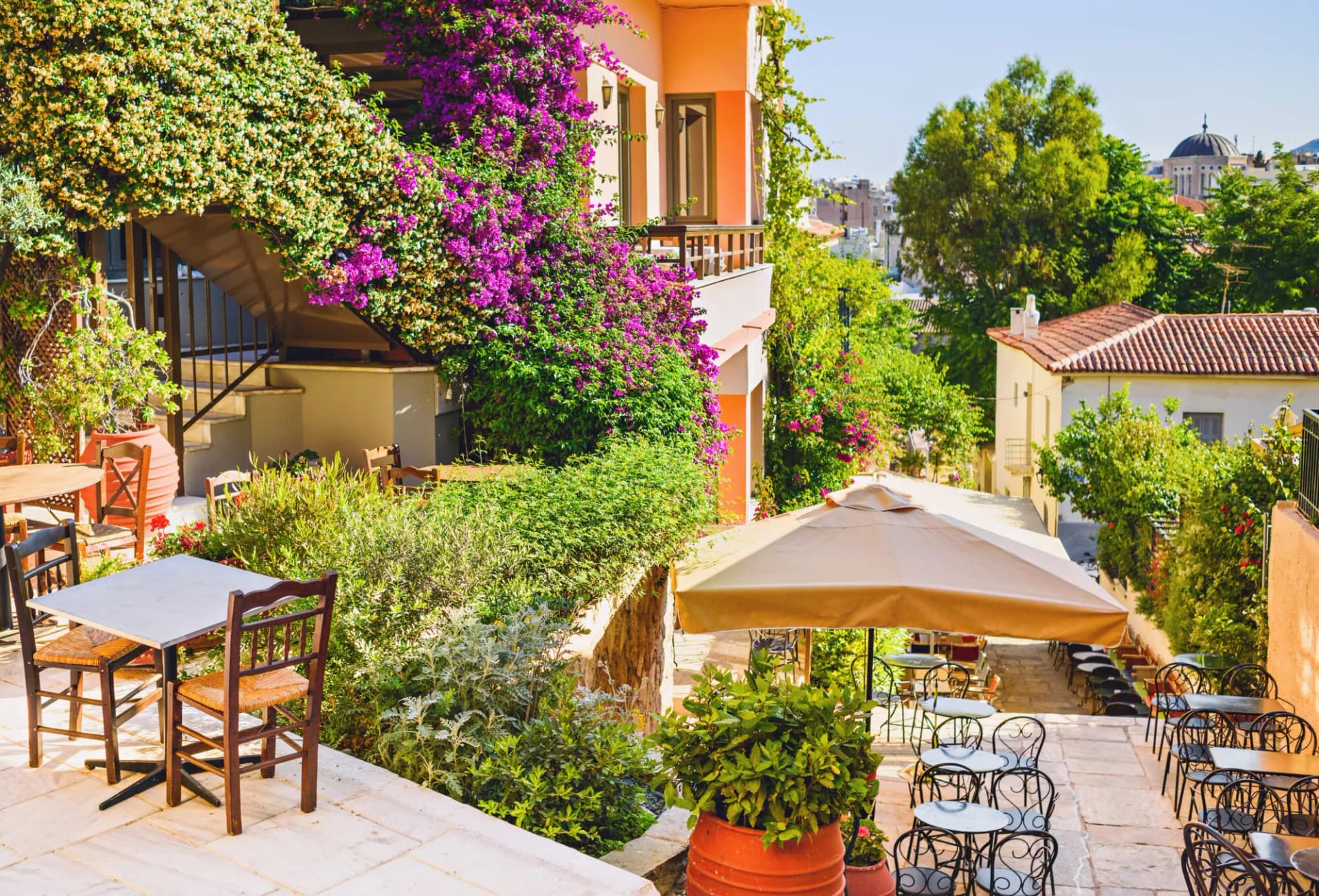 Outdoor cafe seating in Athens Plaka with bougainvillea climbing a peach-colored building.