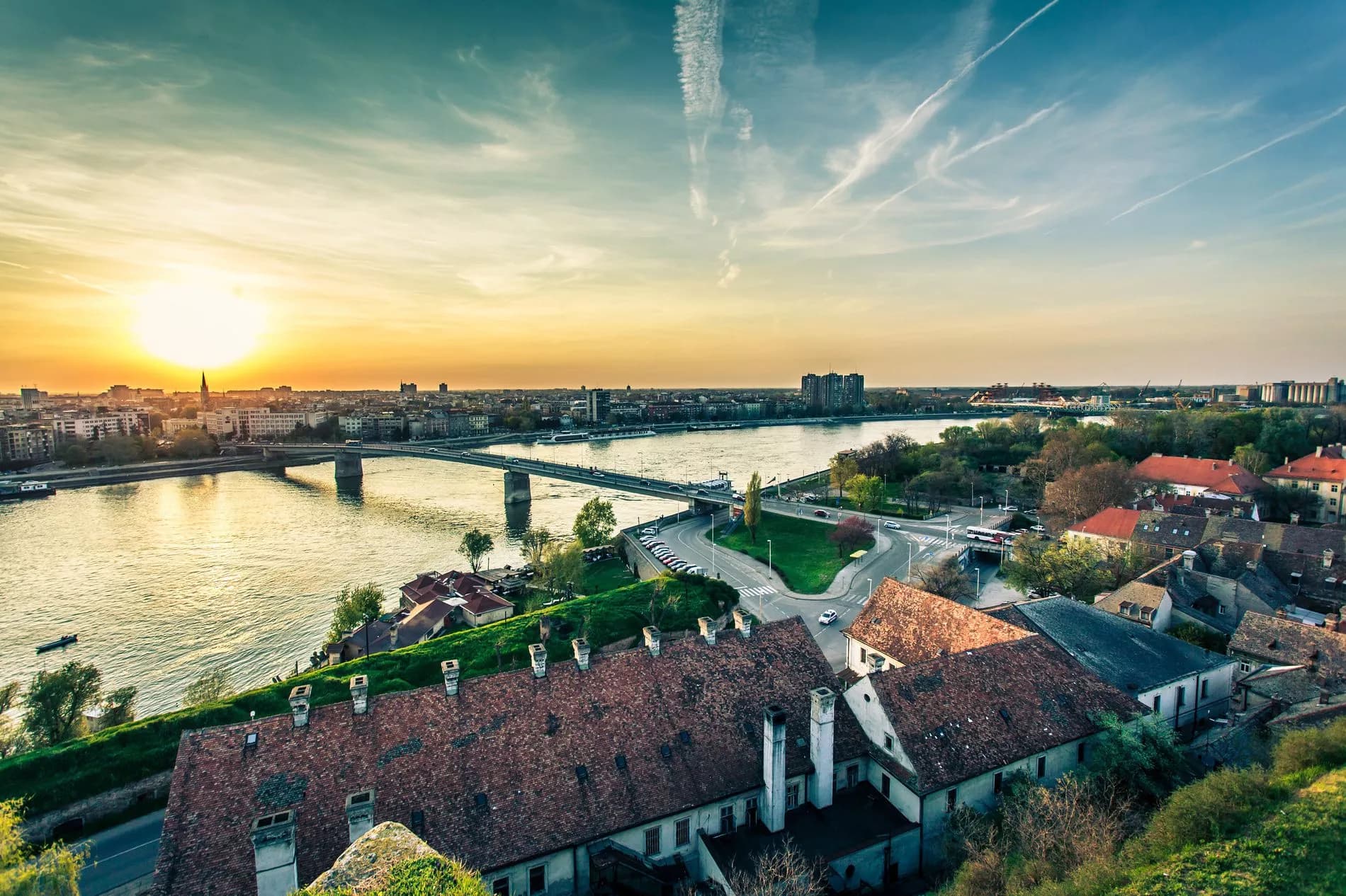 Novi Sad river panorama with bridge, city skyline, and sunset over the Danube River.