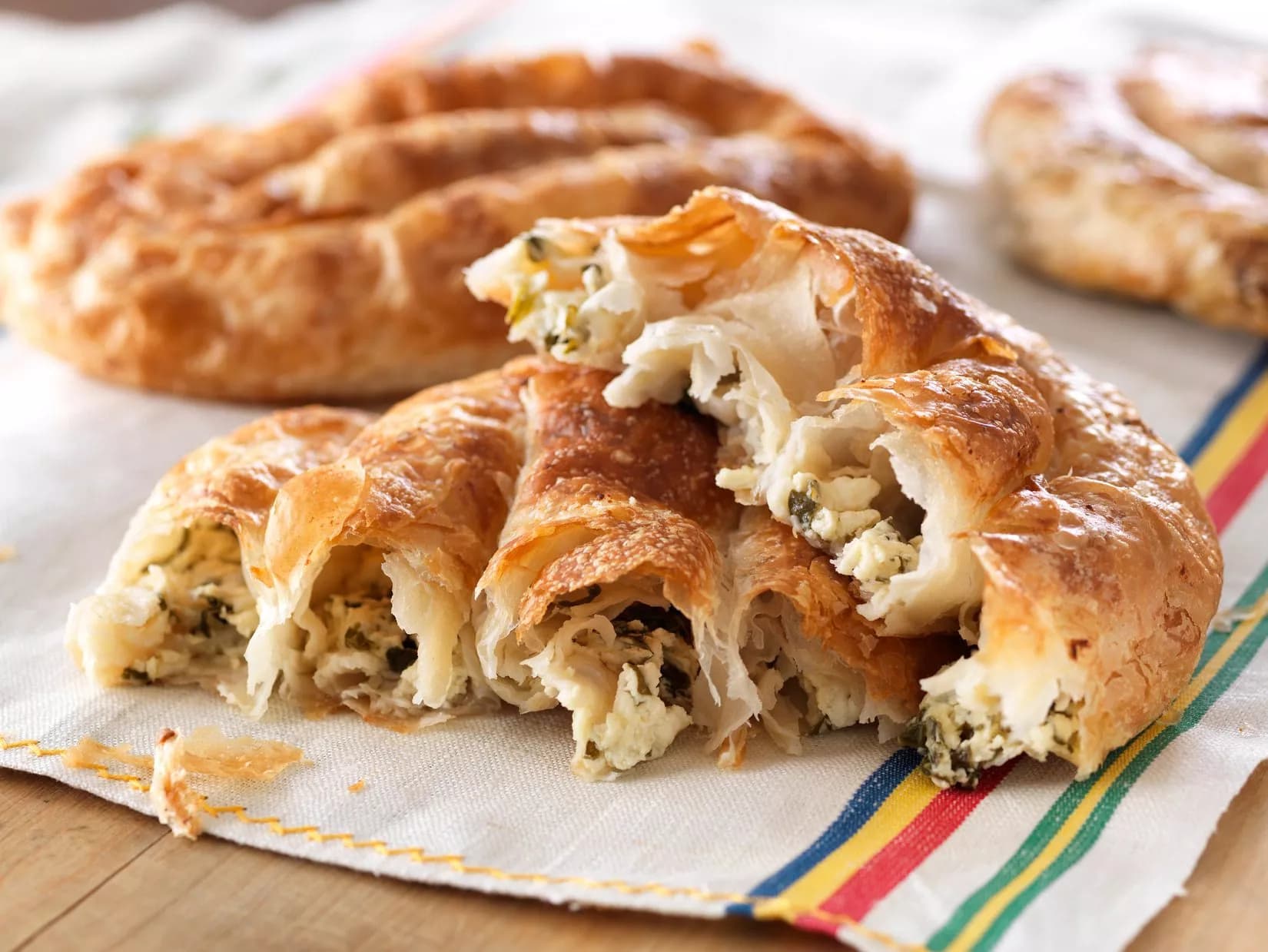 Flaky burek pastry filled with cheese and greens, served on a striped cloth