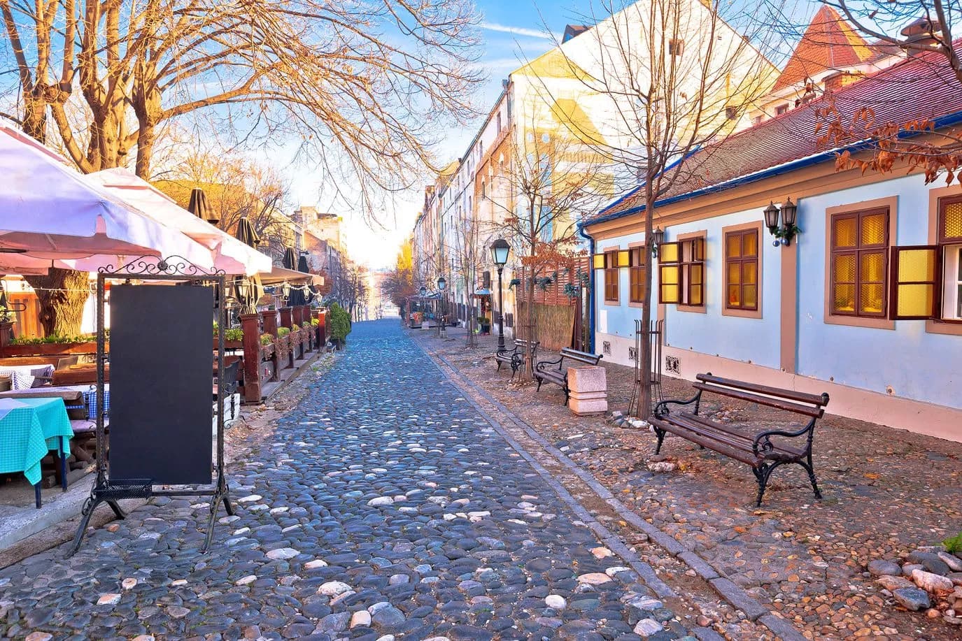 Cobblestone street in Belgrade Skadarlija quarter with outdoor cafe seating and bare trees.