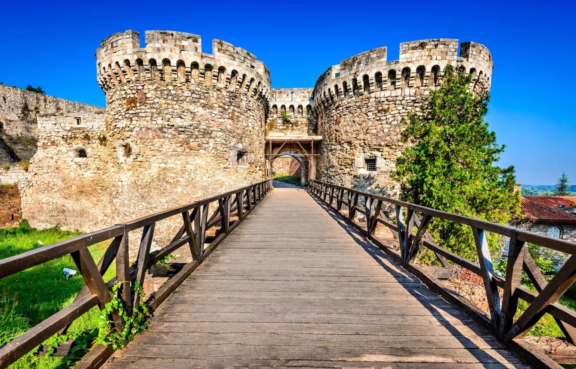 Wooden bridge leading to stone towers of Belgrade Kalemegdan Fortress under a clear blue sky.