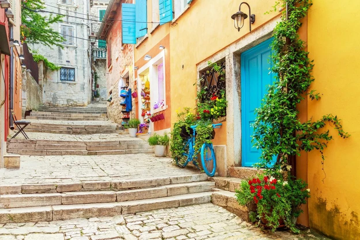 Cobblestone steps leading up a narrow street in Rovinj with colorful buildings and a blue bicycle.