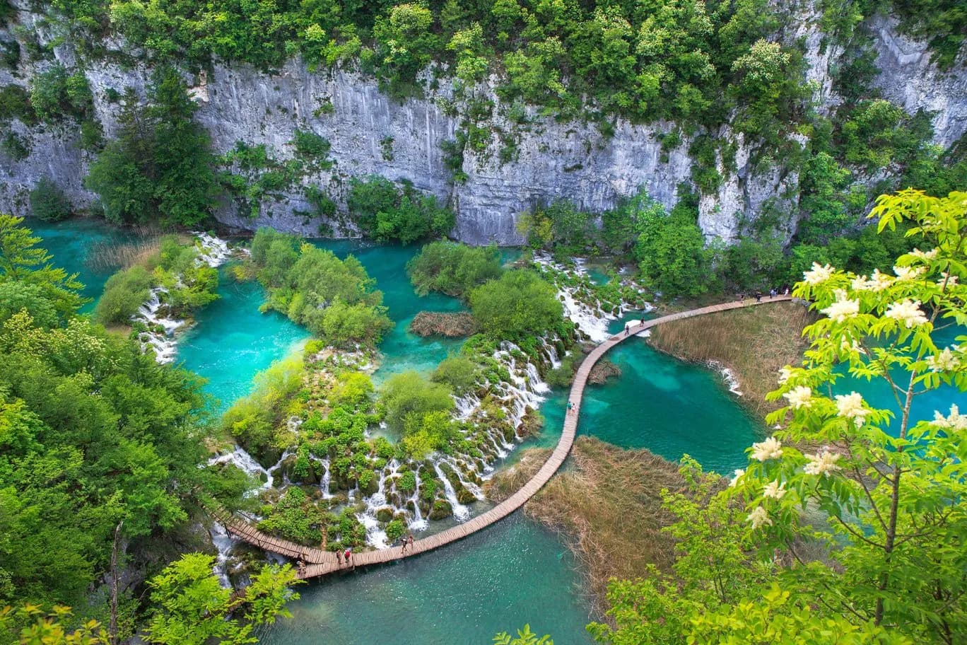 Aerial view of wooden pathways over turquoise water and small waterfalls in Plitvice National Park.