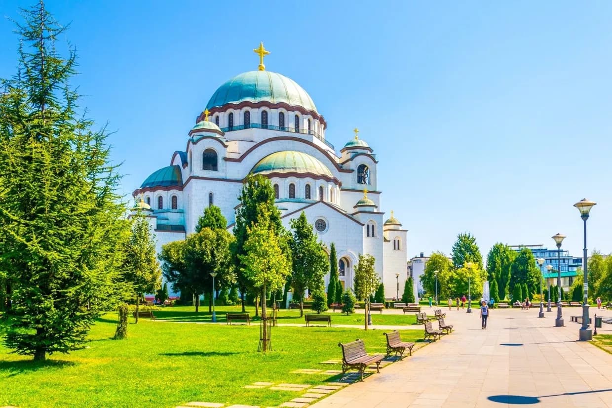 Church of Saint Sava with green domes in park setting under clear blue sky in Belgrade
