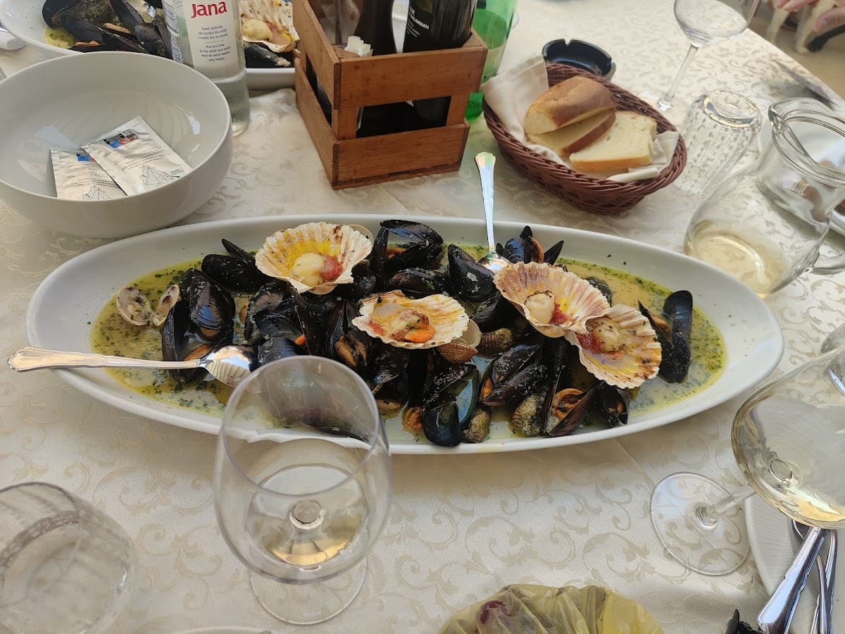 Mussels and scallops in sauce served outdoors with bread, wine glasses, and bottled water.