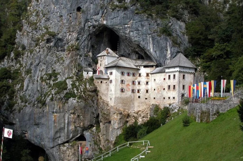 Predjama Castle built into a cliff face with flags displayed on the green hillside.