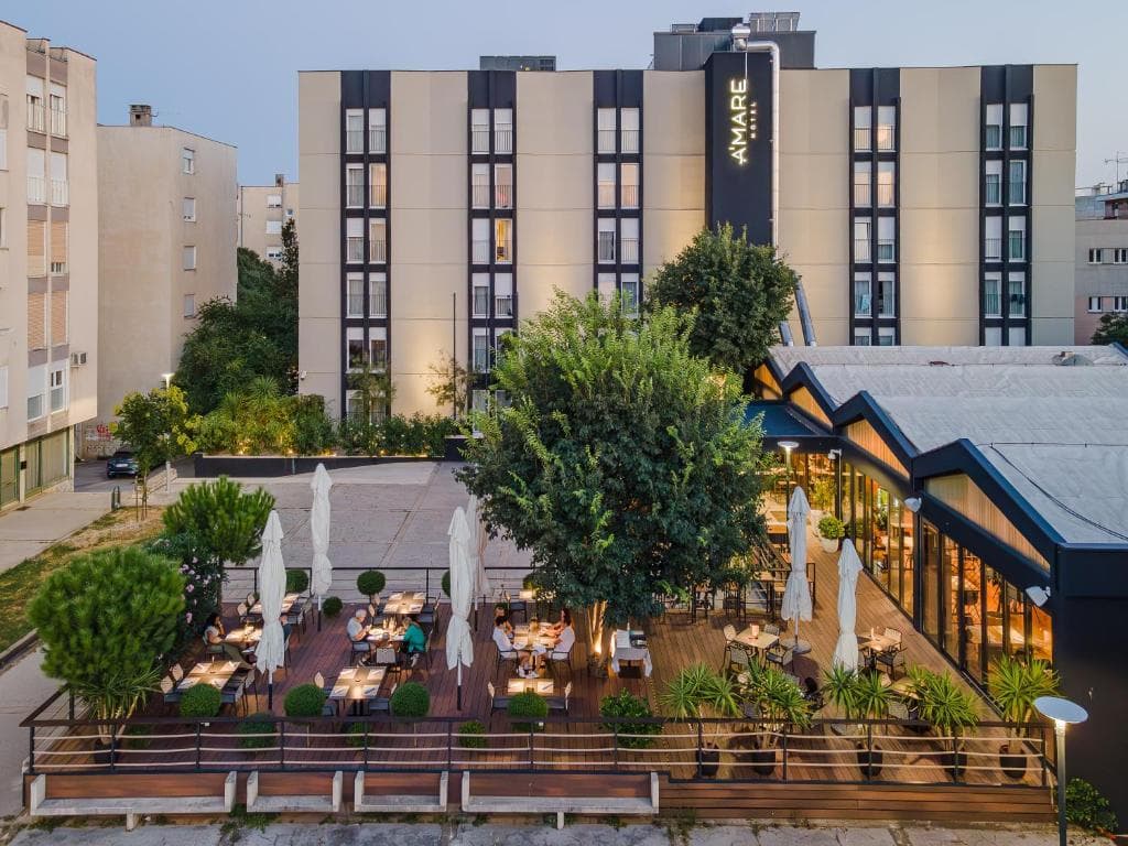 Outdoor dining terrace with tables and umbrellas in front of the Amare Hotel building